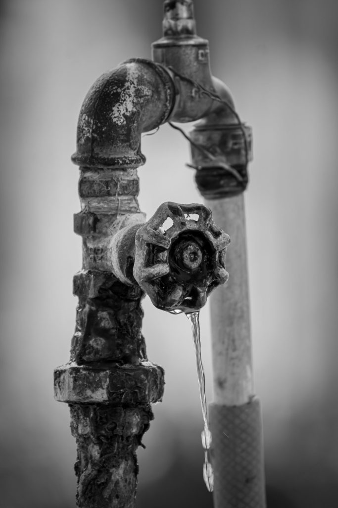 Close-up of an old, rusty faucet dripping water.