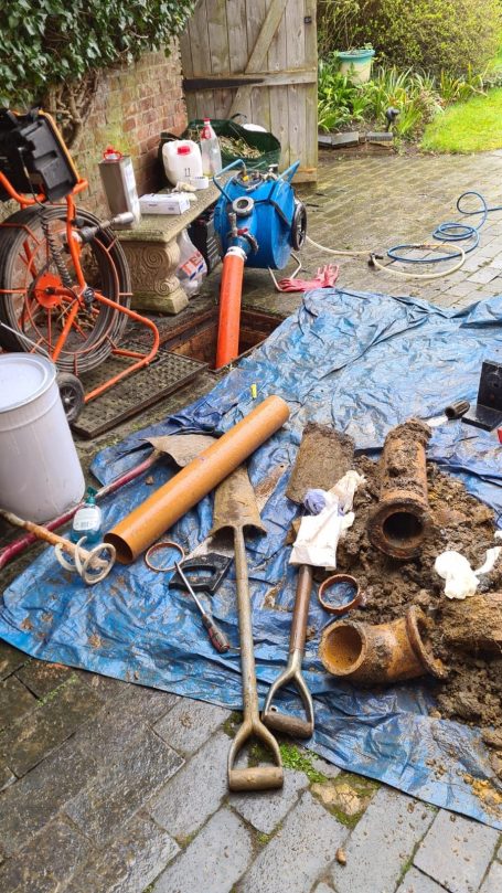 A collection of digging tools and pipes on a blue tarpaulin in an outdoor setting.